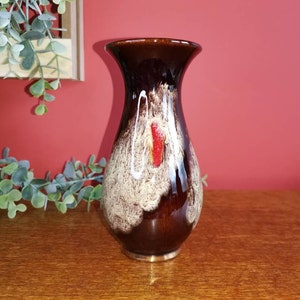 May include: A brown ceramic vase with white and red glaze. The vase has a rounded body and a narrow neck.