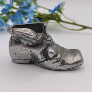 May include: A silver metal shoe shaped trinket. The shoe has a detailed design and a textured surface.