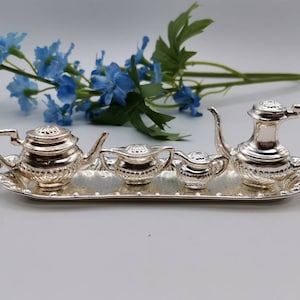 May include: A silver tea set on a silver tray. The set includes a teapot, creamer, sugar bowl, and a small pitcher.