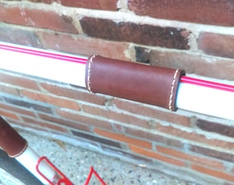 Puede incluir: Un manillar de bicicleta blanco con rayas rojas y una empuñadura de cuero marrón.