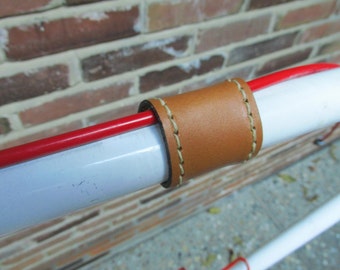 Puede incluir: Primer plano de un tubo de metal blanco con un cordón rojo envuelto alrededor. El tubo está cubierto con una funda de cuero marrón con costuras blancas.