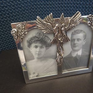 May include: Silver double photo frame with two black and white portraits. The frame has a decorative dove and rose design. A vintage keepsake for displaying cherished memories.