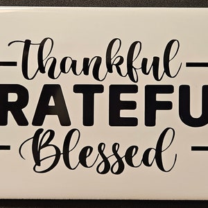 Könnte beinhalten: Weiße Keramikfliese mit schwarzer Beschriftung, die "thankful GRATEFUL blessed" lautet.