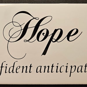 Könnte beinhalten: Weiße Keramikfliese mit schwarzer Schrift in Kursivschrift, die "Hope (confident anticipation)" lautet