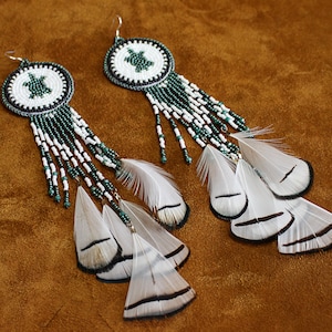 May include: A pair of beaded earrings with green and white beads and white feathers. The earrings feature a turtle design in the center of the beads.