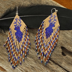 May include: A pair of beaded earrings with a blue deer design and a fringe of brown, beige, silver, and blue beads.