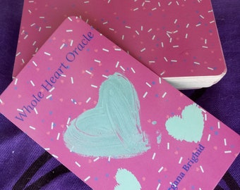 May include: A pink deck of cards with a light blue heart and the text "Whole Heart Oracle" and "Morgana Brighid" on the front.
