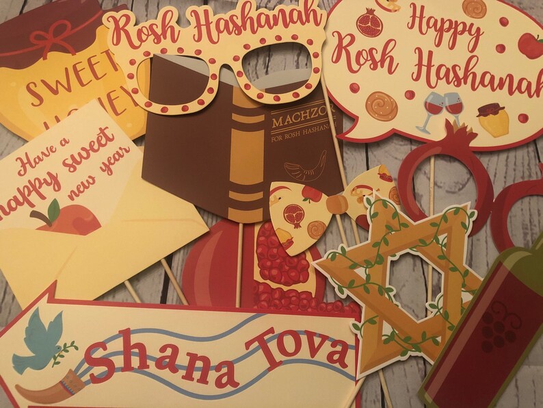 Puede incluir: Accesorios variados para fotomat&oacute;n de Rosh Hashan&aacute; sobre palos de madera. Incluyen gafas, un libro, una granada, una estrella de David y bocadillos con textos como "Happy Rosh Hashanah" y "Shana Tova".