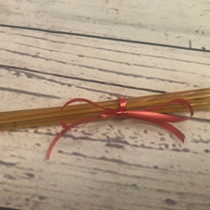 Puede incluir: Un conjunto de palitos de miel atados con una cinta roja. Los palitos, de color &aacute;mbar dorado, est&aacute;n dispuestos en paralelo. La cinta roja brillante a&ntilde;ade un toque decorativo, sugiriendo un regalo o una presentaci&oacute;n cuidada.