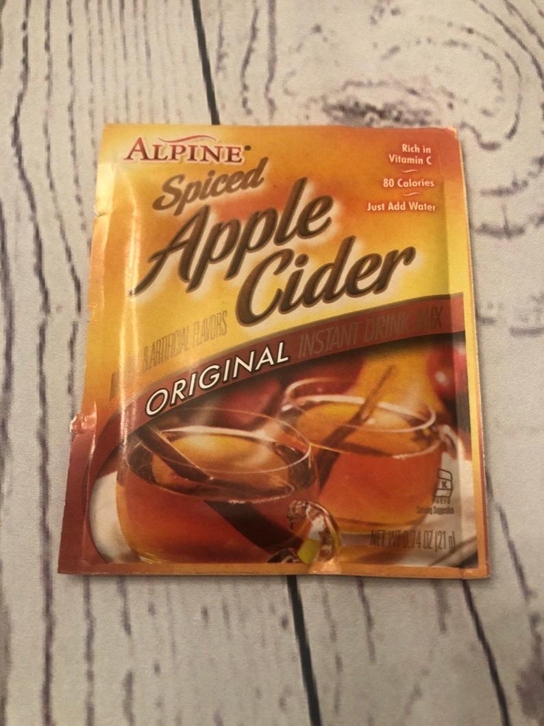 Puede incluir: Un paquete de mezcla de bebida instant&aacute;nea Alpine Spiced Apple Cider. El paquete es naranja y marr&oacute;n con las palabras "Spiced Apple Cider" en letras grandes. Presenta im&aacute;genes de dos tazas de sidra con palitos de canela. El paquete indica "Rich in Vitamin C".
