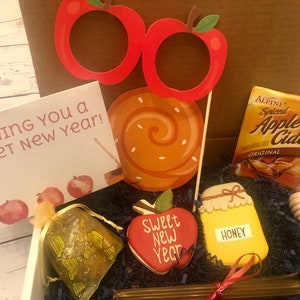 Puede incluir: Una caja de regalo con art&iacute;culos festivos. Incluye una tarjeta que dice "Wishing You a Sweet New Year!", accesorios para fotos con forma de manzana, una piruleta, sidra de manzana, una galleta con forma de miel y un cuchar&oacute;n de miel.