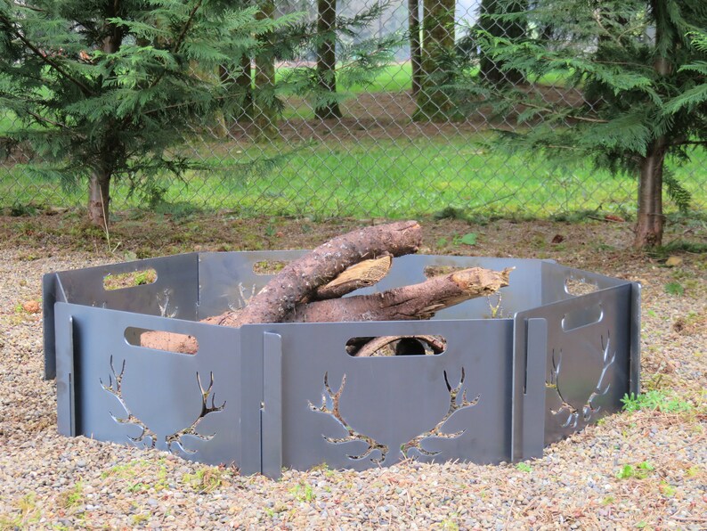 K&ouml;nnte beinhalten: Ein sechseckiger Feuerplatz aus Metall mit einem Hirschgeweih-Design. Der Feuerplatz besteht aus mehreren Paneelen, die sich zusammenbauen und zerlegen lassen. Der Feuerplatz steht auf einer Kiesfl&auml;che.
