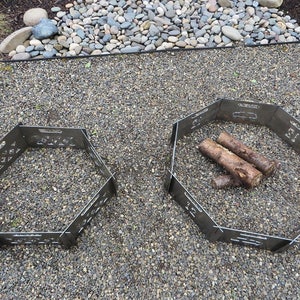K&ouml;nnte beinhalten: Zwei sechseckige Feuerschalen aus Metall, eine mit Holzscheiten darin, auf einer Kiesfl&auml;che.