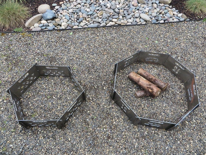 K&ouml;nnte beinhalten: Zwei sechseckige Feuerschalen aus Metall, eine mit Holzscheiten darin, auf einer Kiesfl&auml;che.