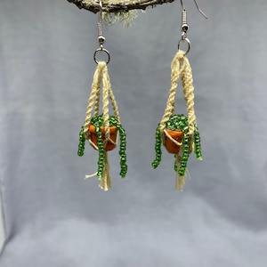 May include: A pair of dangle earrings featuring miniature terracotta pots with green beaded plants hanging from macrame cords.