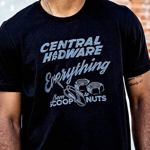 May include: A black t-shirt with a vintage-style graphic that reads "Central Hardware Everything from Scoops to Nuts". The graphic features a wrench and nuts and bolts.