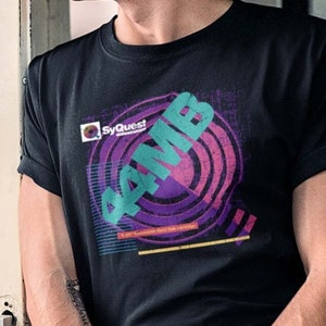 May include: A black t-shirt with a graphic design featuring a circle with concentric rings in shades of purple, pink, and teal. The text "4 MB" is printed in teal and "SyQuest" is printed in white.