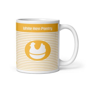 May include: White ceramic mug with a yellow band at the top and a matching band at the bottom. The mug features the text "White Hen Pantry" and a white hen graphic inside a yellow oval. Horizontal yellow lines cover the white surface.