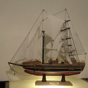 May include: A wooden model ship with white sails, a black hull, and red accents. The ship is on a wooden base with the text "BLUE NOSE" on it.