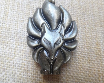 May include: A gold-colored metal pin featuring a stylized nine-tailed fox with a detailed face and fur. The fox is standing on its hind legs with its tail curled around its body.
