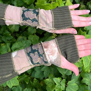 May include: Fingerless arm warmers in shades of olive green, tan, and floral patterns. The arm warmers are made of various fabrics, including ribbed knit and patterned textiles. The design features a mix of textures and colors, with a focus on the olive green ribbed cuffs.