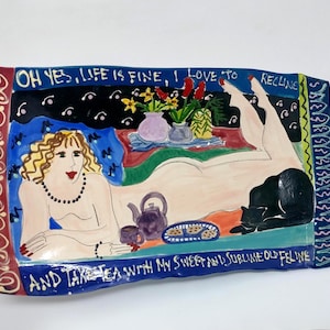May include: A rectangular ceramic tray featuring a hand-painted scene of a reclining figure with blonde hair, a black cat, a teapot, and a plate of cookies. The text reads: OH YES, LIFE IS FINE, I LOVE TO RECLINE AND TAKE TEA WITH MY SWEET AND SUBLIME OLD FELINE.