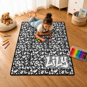 Pode incluir: Um tapete retangular com um padrão repetitivo em preto e branco de gatos, arco-íris, donuts e estrelas. O tapete inclui o nome Lily numa fonte grande e arrojada com contorno branco no canto inferior direito para ser colorido.