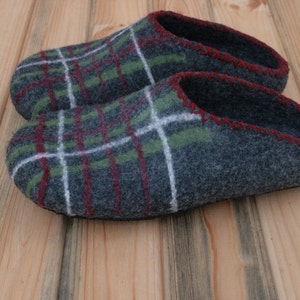 May include: A pair of gray wool slippers with a green, red, and white plaid pattern. The slippers have a red stitched edge and a black rubber sole.