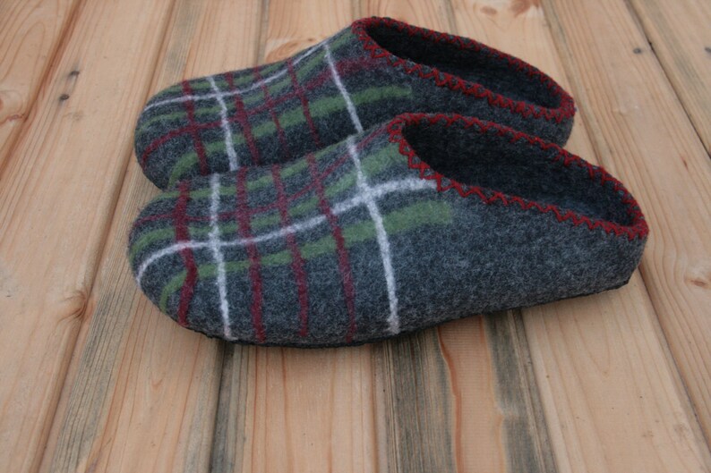 May include: A pair of gray wool slippers with a green, red, and white plaid pattern. The slippers have a red stitched edge and a black rubber sole.