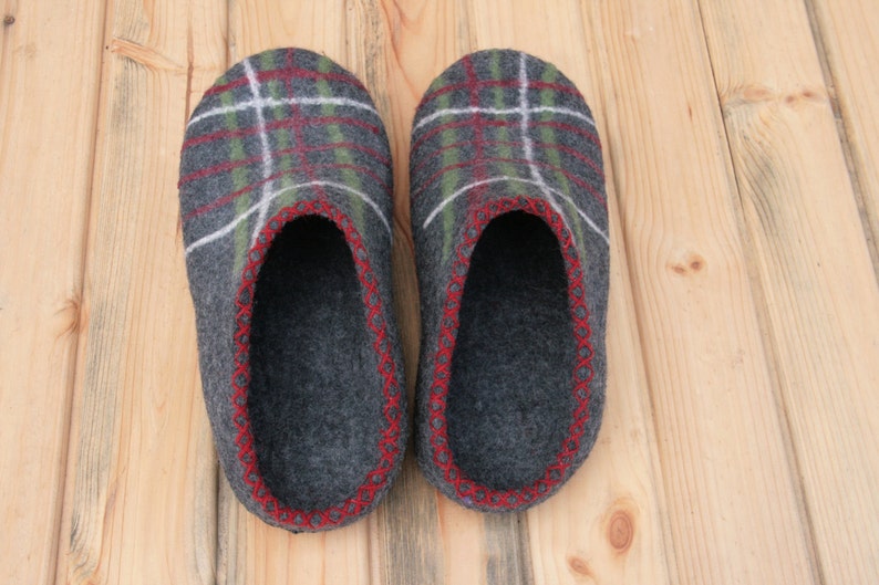 May include: A pair of gray wool slippers with a red and green plaid pattern. The slippers have a red stitched trim around the edges.