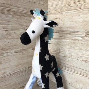 May include: A black and white stuffed giraffe toy with blue and white striped legs and a blue and white striped mane. The giraffe has a white face with black eyes and a black nose. The giraffe is standing on a wooden surface.