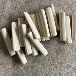 以下が含まれることがあります： オフホワイトの滑らかな長方形の骨のようなピースの山。ピースはランダムなパターンで配置されています。