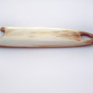 May include: A bone knitting needle with a light brown and white colour pattern. The needle has a small hole at the end.