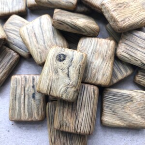 Könnte beinhalten: Eine Sammlung kleiner, rechteckiger Holzfliesen mit natürlicher Holzmaserung und dunkelbraunen Streifen. Die Fliesen haben ein rustikales, handgemachtes Aussehen.