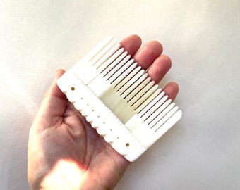 May include: White plastic comb with a row of teeth on one side and a row of small holes on the other side.