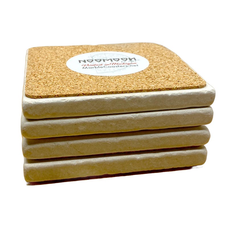 May include: A stack of six square cork-backed coasters with a white ceramic base. The top coaster has a round sticker with the text "Noomoo" and "Printed in Michigan MarbleCoasters.net".