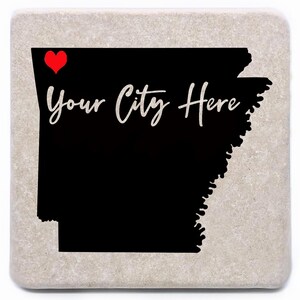 May include: A square stone coaster featuring a black silhouette of the state of Arkansas. A red heart is above the state outline, and the words "Your City Here" are written in white script.