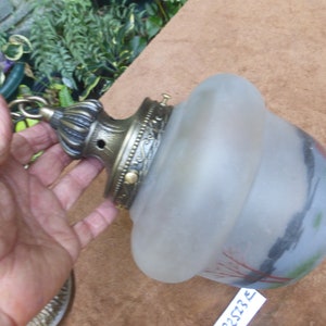 Może przedstawiać: Wisząca lampa z matowego szkła z łańcuchem mosiężnym i ozdobnym mosiężnym mocowaniem sufitowym. Klosz szklany ma malowany wzór z czerwonymi, zielonymi i czarnymi akcentami.