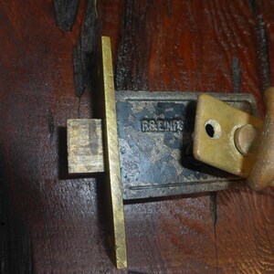 May include: A vintage brass door latch with a black metal plate. The plate has the inscription "R&E MFG".