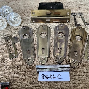 May include: A collection of antique door hardware including four clear glass knobs with star patterns, brass rectangular backplates, two metal keys, a black mortise lock box, and two metal spindles. A white label displays the handwritten text 81626 C.