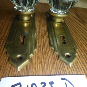 May include: Two antique brass door knobs with clear glass crystal knobs. The knobs have a keyhole and are in good condition. The image also includes a handwritten note with the number 71023 D.