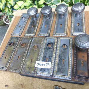 Puede incluir: Un conjunto de herrajes de puerta antiguos, que incluyen varios pomos y placas traseras a juego. Los pomos son redondos con un diseño decorativo. Las placas son rectangulares con cerraduras y bordes ornamentados. El texto "71224 P" es visible.