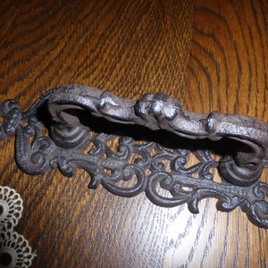 以下が含まれることがあります： 装飾的な装飾が施された黒い鋳鉄製のドアノッカー。ノッカーにはリングプルハンドルと、詳細なスクロールのようなパターンがあります。