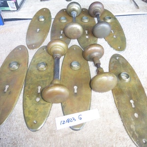 May include: A collection of 10 antique brass door knobs and backplates. The knobs are oval shaped and have a keyhole. The backplates are also oval shaped and have a smooth surface. The knobs are all in good condition and have a nice patina.