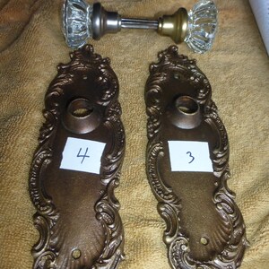 Peut inclure: Deux plaques de porte en laiton ornées d'un motif décoratif. Les plaques sont numérotées "3" et "4".