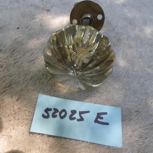 May include: A clear, ribbed glass doorknob with a brass mounting plate. The doorknob has a rounded shape with a textured surface. A blue tag with the text "52025 E" is in the image.
