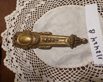 May include: A gold-toned metal decorative piece with an oval centre and intricate floral designs. The piece has a slightly aged look and is about 15 cm long.