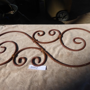 Puede incluir: Una pieza decorativa de metal oxidado con un diseño de espiral. La pieza está sobre una superficie de tela beige. El número 3222 C está escrito en una etiqueta blanca.