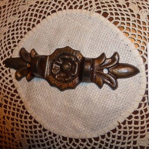 Könnte beinhalten: Ein brauner Wandhaken aus Metall mit einem dekorativen Blumendesign. Der Haken hat eine einzelne Spitze und ist an einer Wand befestigt.