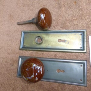 Puede incluir: Dos pomos de puerta antiguos con placas traseras a juego. Los pomos son de color marrón brillante y las placas traseras son rectangulares con recortes para cerraduras. También hay una etiqueta blanca con el texto "92823 T".